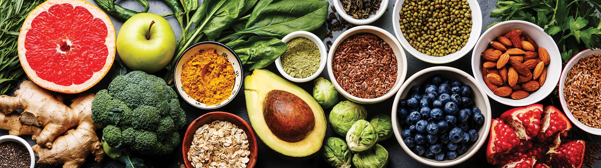 An assortment of fresh foods including avocado, spinach, apple, broccoli, oats, turmeric, flax seeds, mung beans and much more.